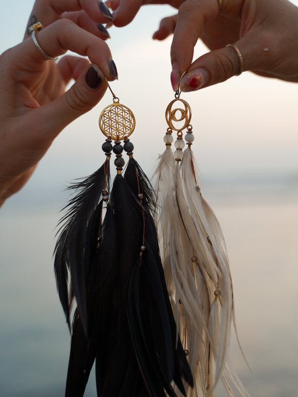 Two hands holding up a black Flower of Life pair and a white Vesica Piscis pair against a soft sunset sea