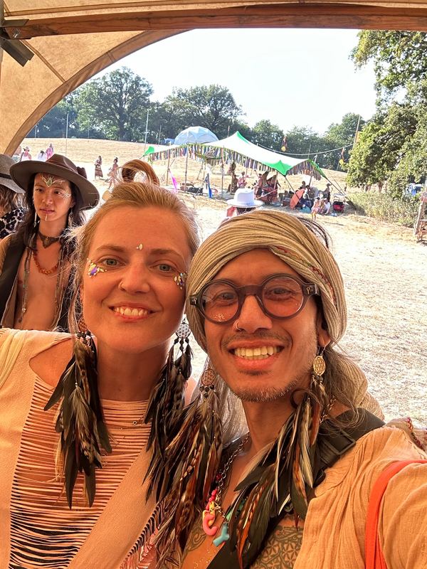 Two friends at a festival tent, both wearing long dark feather earrings