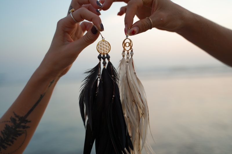 Two hands holding up a black Flower of Life pair and a white Vesica Piscis pair against a soft sunset sea