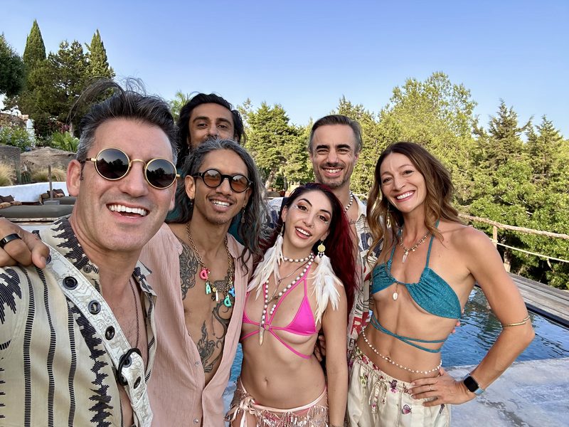 Friends gathered by a pool on a sunny day, one wearing white feather earrings with a gold charm and another a white leather holster strap
